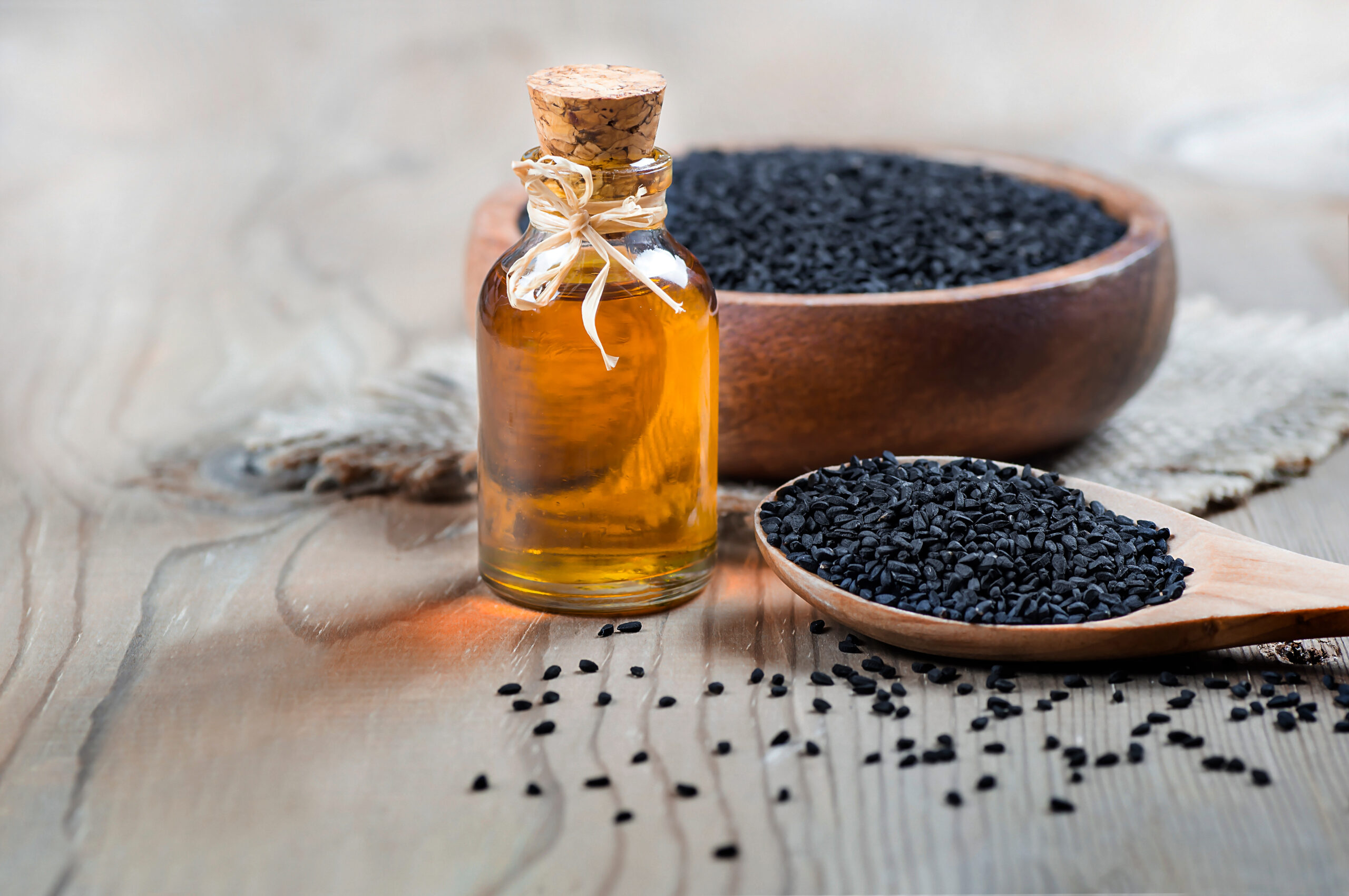 glass container with black seed oil sitting in front of a bowl of black seeds