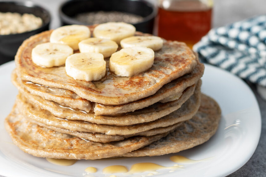 stack of pancakes made with oat flour topped with bananas sitting on a white plate