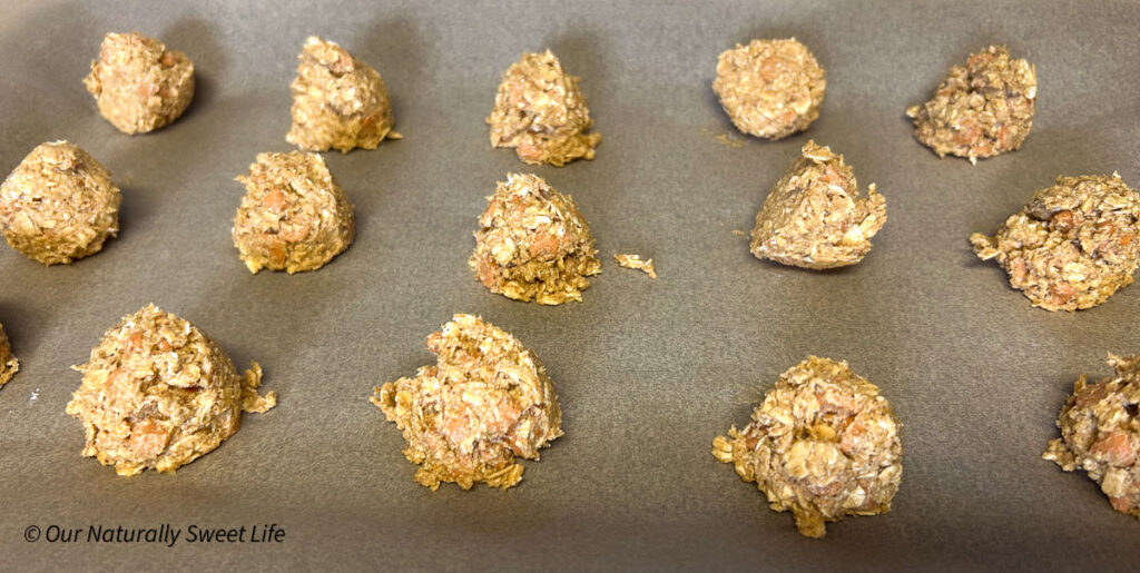 Scoops of unbaked sugar-free butterscotch oatmeal cookie dough arranged on a parchment-lined baking sheet, ready to go into the oven. The dough is chunky with visible oats and butterscotch chips, made with wholesome, low-glycemic ingredients.
